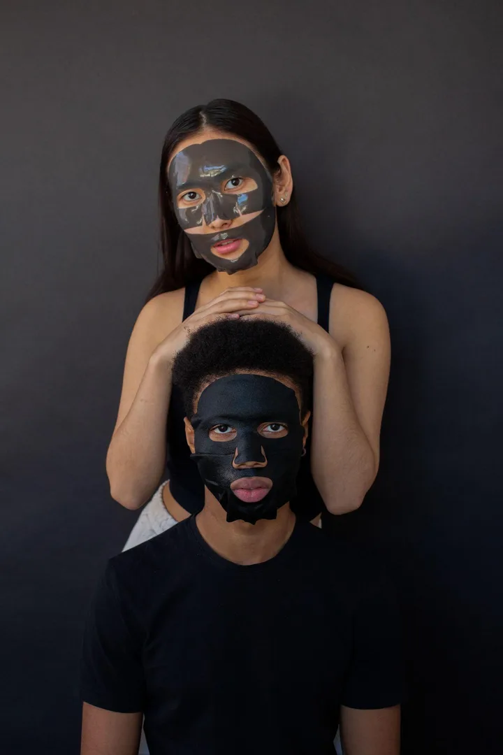 Dve osoby s tmavými pleťovými maskami na tvári na tmavom pozadí